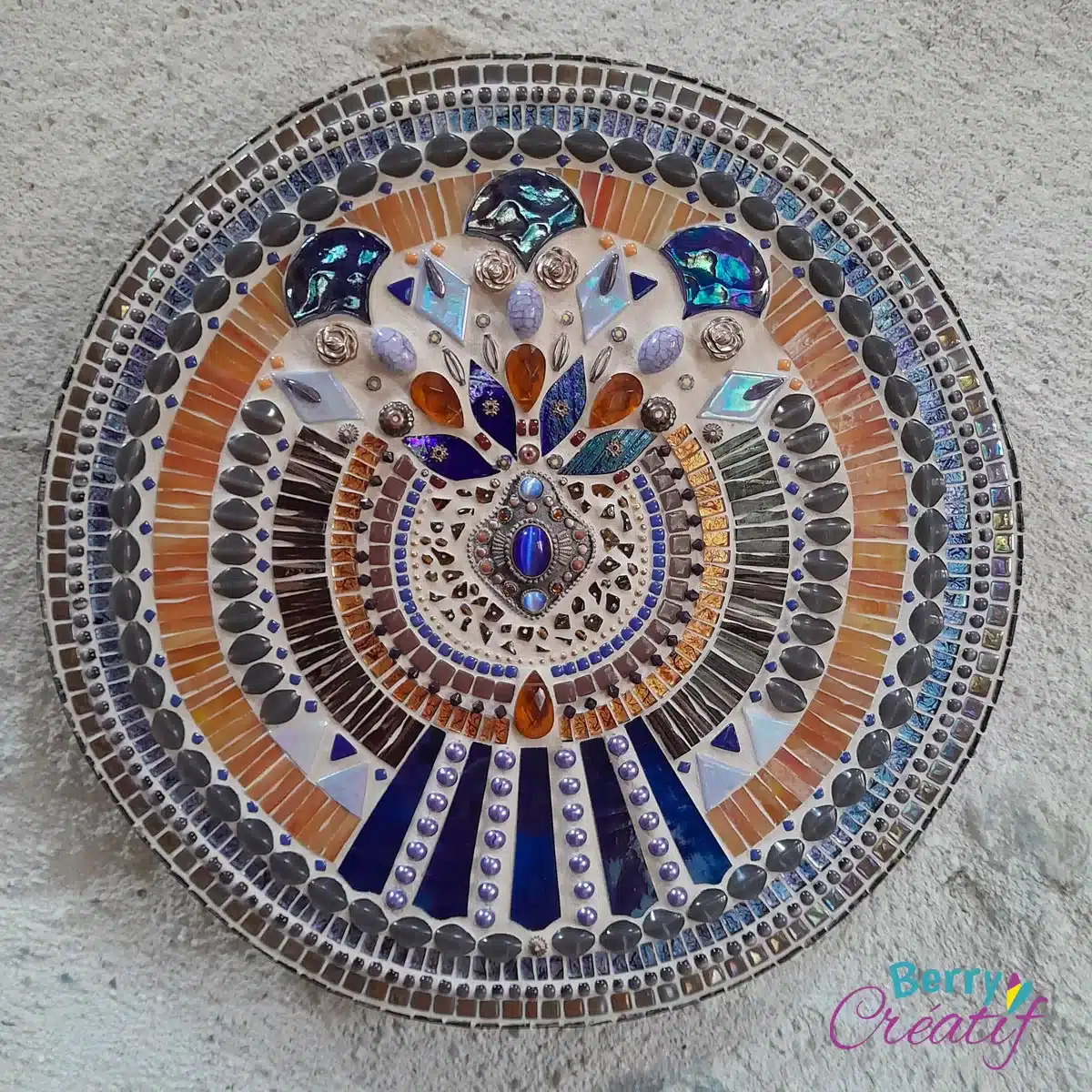round mosaic art with indigo blue and orange colours and old jewellery