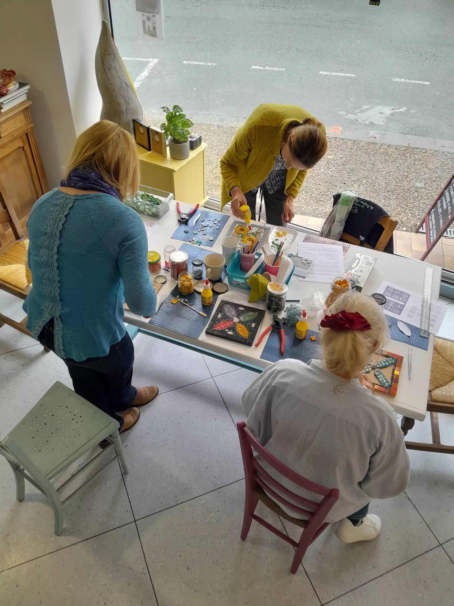 photo looking down on the craft toable with three people working around it, making mosaics