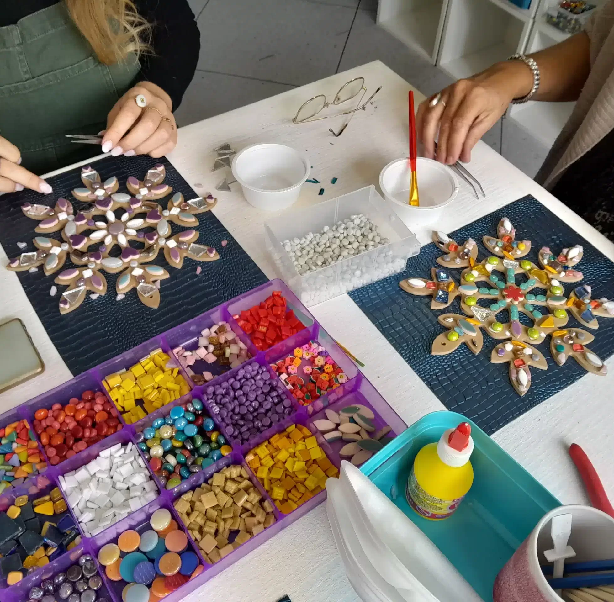 a craft table full of coloured mosaic tiles and large snowflakes being made