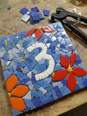 a square mosaic house number sign showing a white number three and some flowers with a blue background